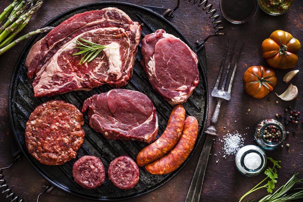 Various cuts of raw meat on a cast iron grill